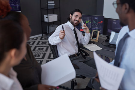 Young smiling broker selling the stocks successfully to customer during conversation by the phone