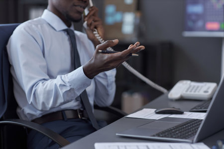 Close-up of African American broker talking on the phone with customer while sitting at his workplace with laptopの写真素材