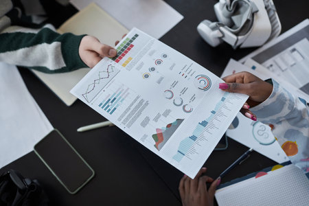 High angle view of colleagues examining document with graphs at table during meeting in office