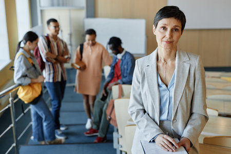 Portrait of mature teacher in elegant suit looking at camera while standing in lecture hall after...