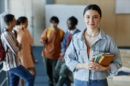 POrtrait of young woman standing with books in lecture hall with other students in backgroundの写真素材