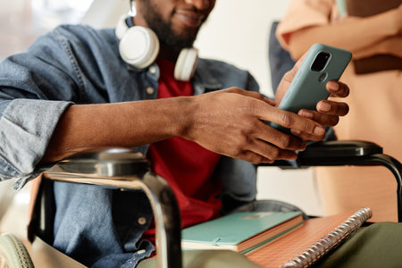 Close-up of student with disability sitting on wheelchair and communicating online with smartphone...