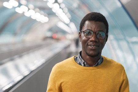 Portrait of African American man in eyeglasses smiling at camera while standing on escalator in...