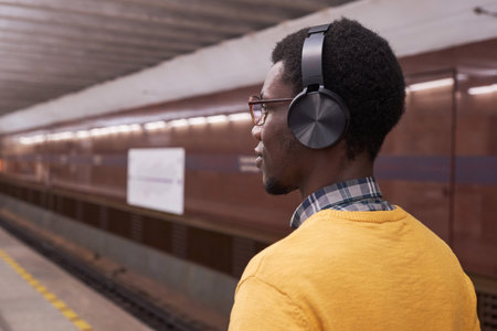 Rear view of African American man in wireless headphones listening to music standing in station in undergroundの写真素材