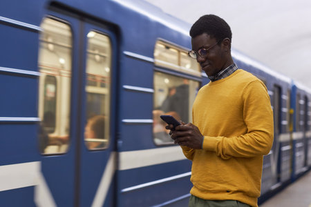 African American man using smartphone standing on station in undergroundの写真素材