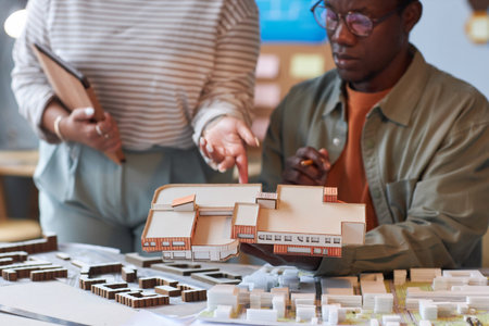 Close-up of young colleagues discussing the mockup of new building during teamwork in officeの写真素材