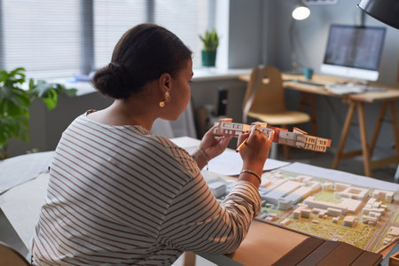 Rear view of African American woman working over new project of building sitting at her workplace