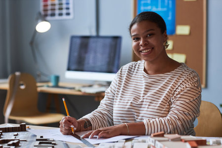 Portrait of African American architect smiling at camera while drawing blueprint at table