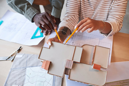 High angle view of architects drawing model of building in team sitting at table with blueprint and...