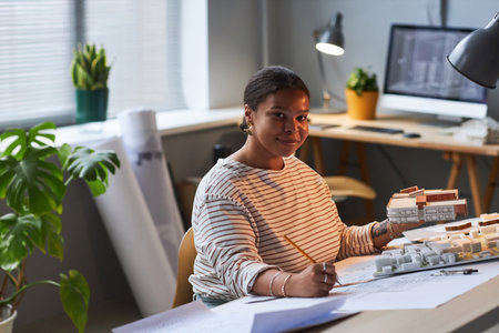 Portrait of young architect looking at camera while working at her workplace and developing new mockups of buildingの写真素材