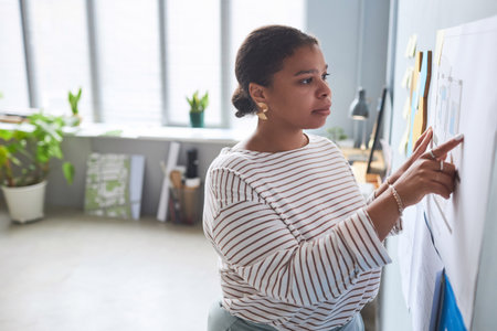 African American woman examining plan on the wall during her work in officeの写真素材