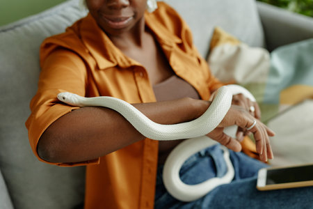 Close-up of white rat snake creeping over arms of young African American female owner holding exotic pet during animal assisted therapyの写真素材