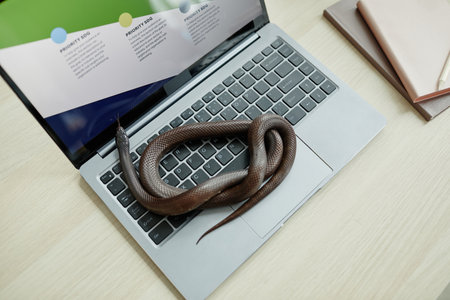 High angle of twisted rat snake creeping over keyboard of laptop with online graphic financial data...