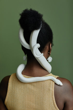 Back view of young African American woman with white rat snake enlacing her hair bun standing in...