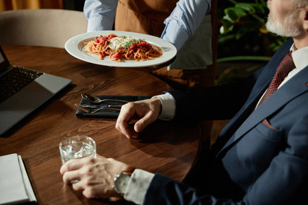 Close-up of waiter serving pasta for businessman during lunch time in restaurantの写真素材