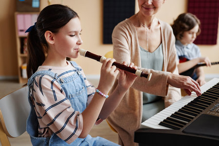 Schoolgirl playing flute with teacher playing piano during musical lesson in classの写真素材