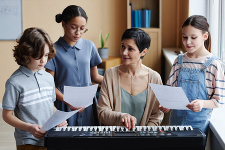 Mature teacher playing piano and rehearsing song with children while they standing with notes around her in music classの写真素材