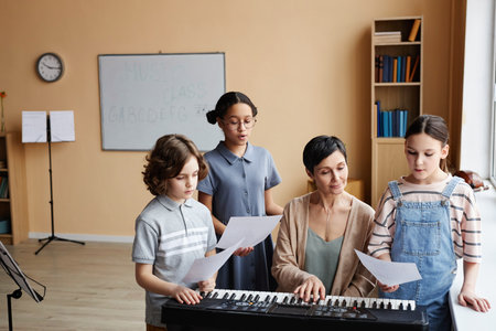 Group of children reading notes and singing songs while teacher playing piano during music lesson in classの写真素材