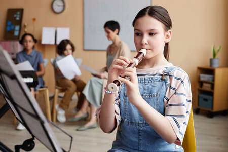 Schoolgirl sitting in front of sheet music and learning to play flute in music classの写真素材