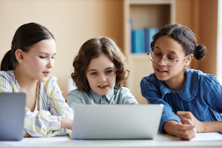 School children using laptop to watch video together while sitting at table in classの写真素材