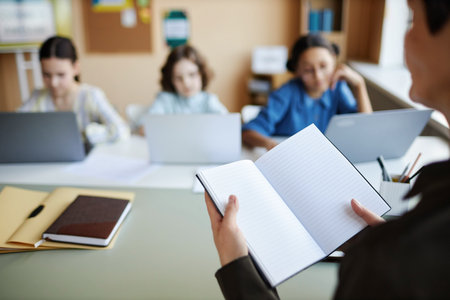 Close-up of teacher opening her notebook and giving homework to children during lessonの写真素材