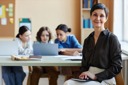Portrait of mature teacher looking at camera sitting at lesson with children in backgroundの写真素材