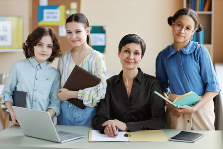 Portrait of mature teacher looking at camera together with her students while teaching lesson in...