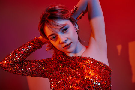 Portrait of young beautiful woman posing in shiny red dress against colored background
