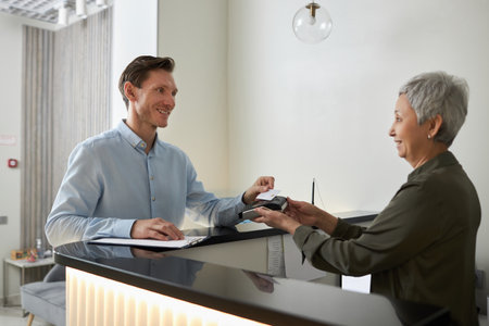 Portrait of smiling elegant man paying in medical clinic via NFC technology, copy spaceの写真素材