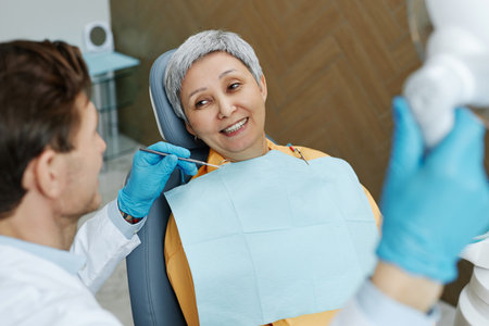 Portrait of smiling senior woman in dental clinic sitting in chair and looking at male dentist.