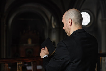 Rear view of pastor in black suit standing with Bible and praying in churchの写真素材