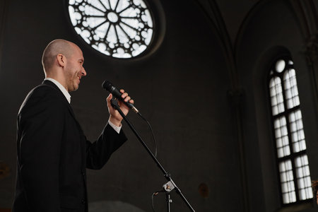 Mature pastor in black suit speaking prayer in microphone while standing in old baptist churchの写真素材