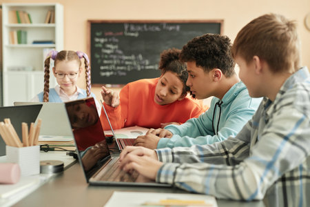 Diverse group of children using laptops in school classroom with black girl peeking at computer...