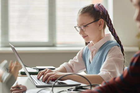 Side view portrait of smiling cute schoolgirl using laptop in programming class for childrenの写真素材