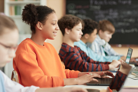 Side view at black teenage girl using computers in row in school classroom and taking online examの写真素材