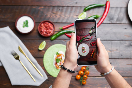 Top view of man making photo of food on wooden table on mobile phone for food blogの写真素材