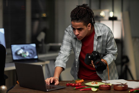 Professional photographer connecting camera to laptop while making professional photos of food on table in studioの写真素材