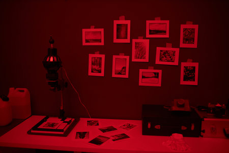 Workplace with equipment and photos on table in darkroom with red light