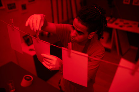 Young photographer hanging printed photos during his work in darkroom