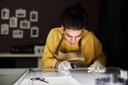 Young photographer watching photo film with magnifier by putting it on lightbox