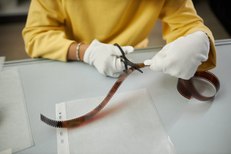 Close-up of photographer in white gloves cutting photo film with scissors while sitting at his workplaceの写真素材