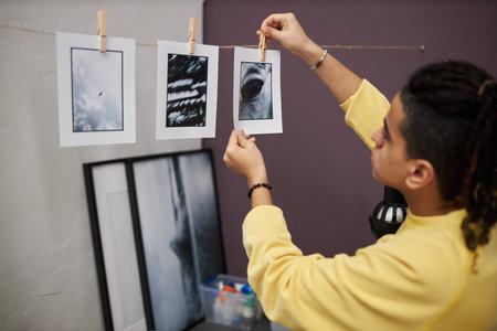 Young photographer printing black and white photos and hanging ready photos on rope while working in photo studioの写真素材