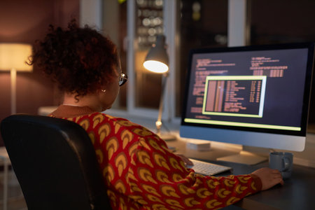 Rear view of female programmer sitting at her workplace in front of computer monitor and working...