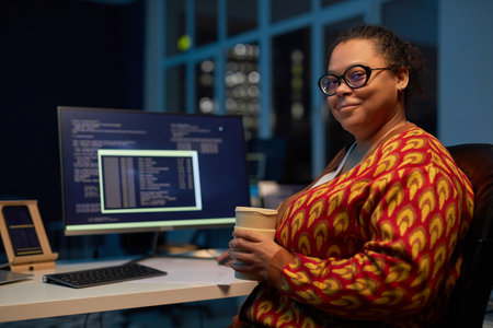 Portrait of African American woman with coffee cup looking at camera while working in IT office till late eveningの写真素材