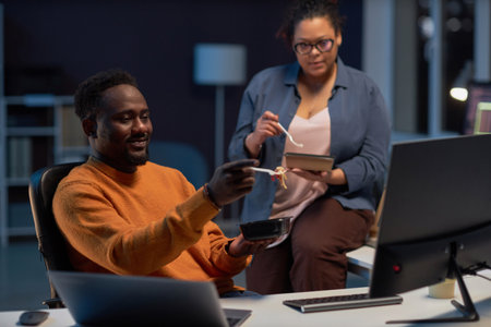 Programmers having lunch and working over computer program till late night in IT officeの写真素材