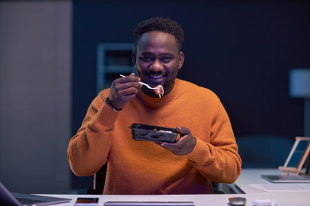 Portrait of African American programmer smiling at camera while having lunch at workplace in IT...