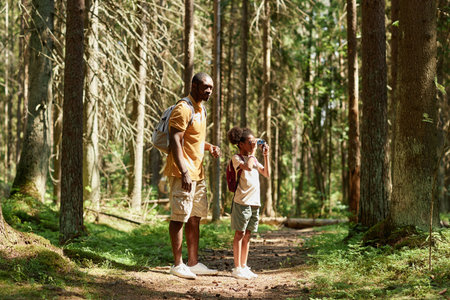 Little girl looking through binoculars during travelling with her dad in the forestの写真素材