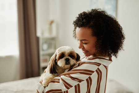 Minimal side view portrait of black young woman holding cute pet dog at home and smilingの写真素材