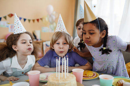 Diverse group of happy children blowing candles on cake together during birthday partyの写真素材
