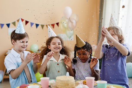 Diverse group of excited little kids throwing confetti while enjoying birthday party for children...